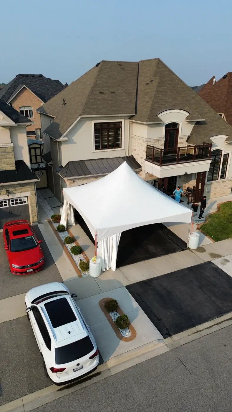 A white rental tent installed on a residential driveway for an outdoor gathering